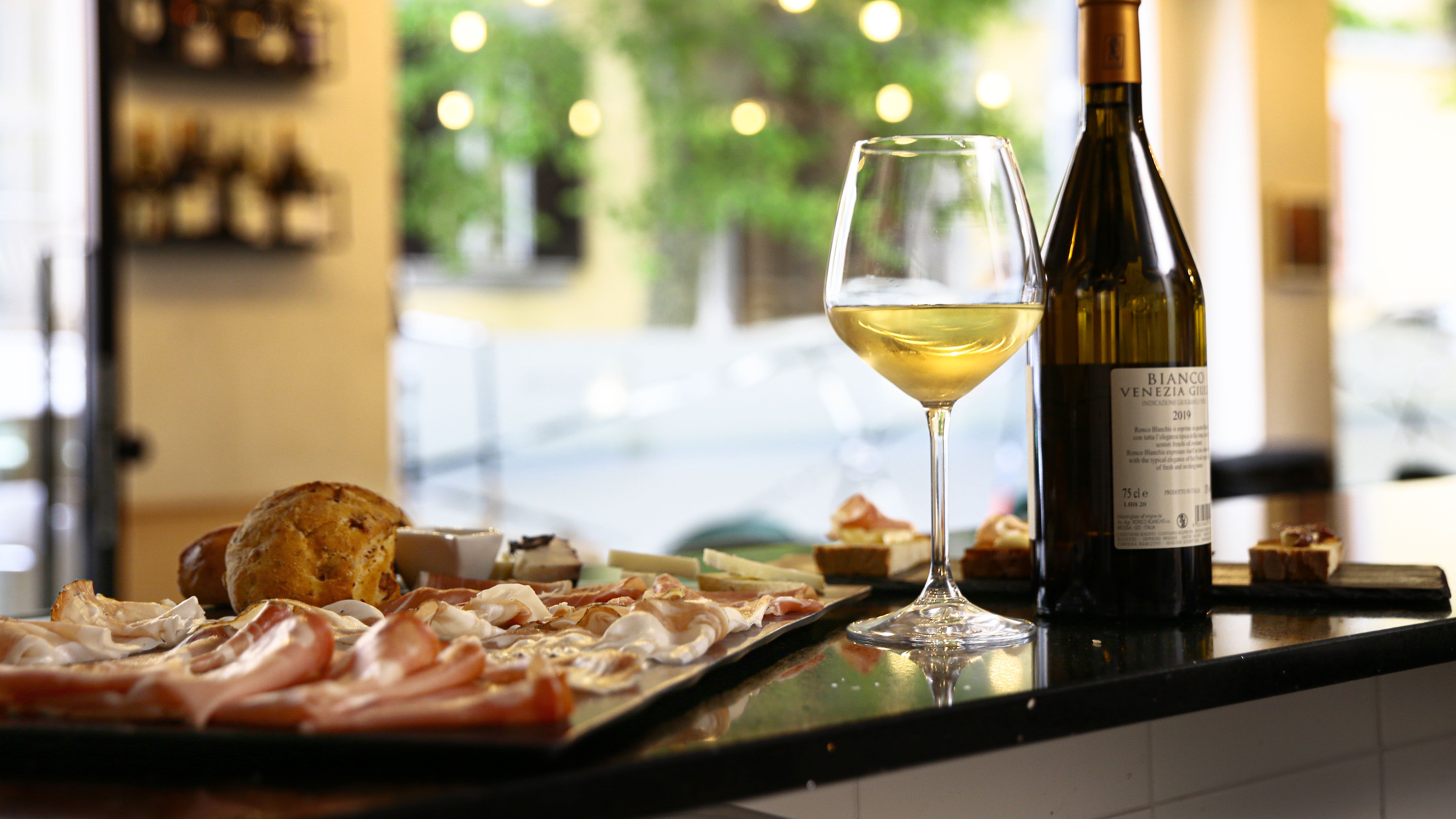 Calice di vino bianco, bottiglia e selezione di salumi al bancone di Symposium